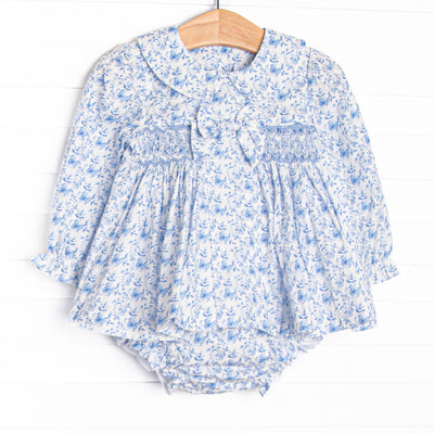 This set features a blue floral fabric, dainty smocking, a floral peter pan collar, and a pre tied bow.