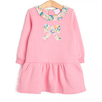 This sweatshirt dress features pink knit fabric, floral ruffle trim, and a floral bow applique. 