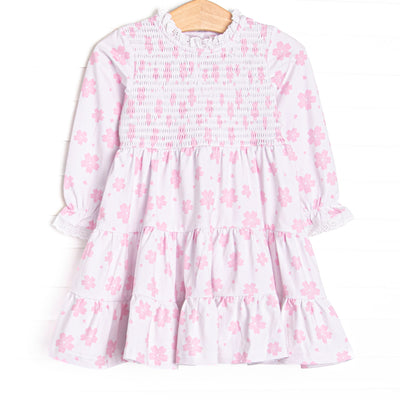  This dress features pink floral print, chest smocking, and eyelet lace trim. 
