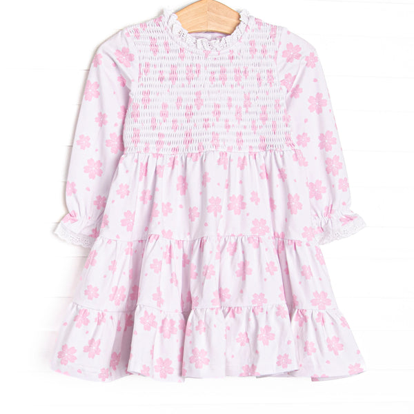  This dress features pink floral print, chest smocking, and eyelet lace trim. 