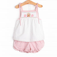 This set features a swiss dot top with a castle smocking and shoulder ties. Coordinating pink gingham ruffle shorts to match.