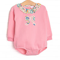 This sweatshirt bubble features pink knit fabric, floral ruffle trim, and a floral bow applique.