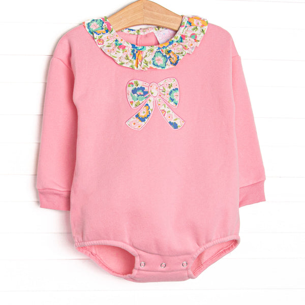 This sweatshirt bubble features pink knit fabric, floral ruffle trim, and a floral bow applique.