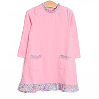  This dress features pink knit fabric, front ruffle pockets, and floral ruffle trim. 