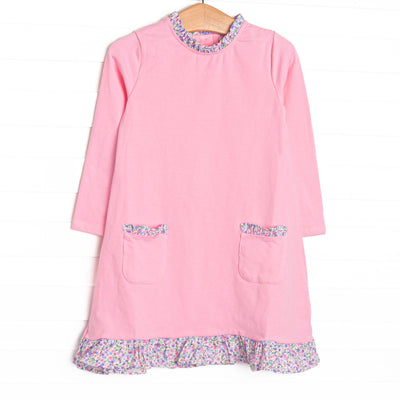  This dress features pink knit fabric, front ruffle pockets, and floral ruffle trim. 