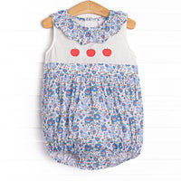 This bubble features a blue floral print, a ruffle collar, and a trio of apple appliques.