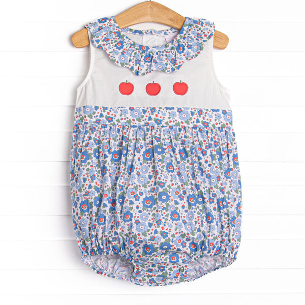 This bubble features a blue floral print, a ruffle collar, and a trio of apple appliques.