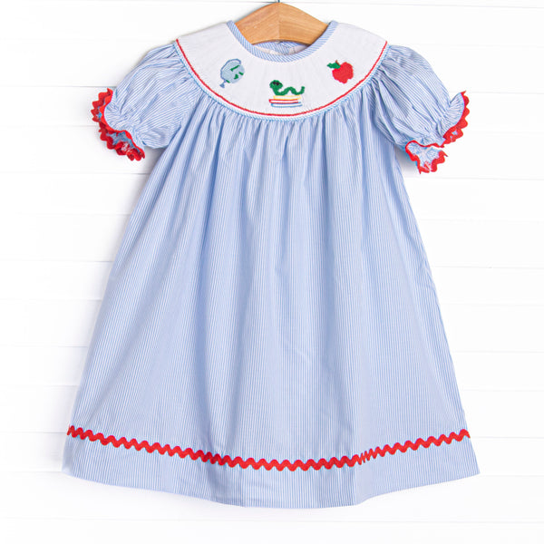 This dress features a blue striped print, red ric rac trim, and a school smocking.