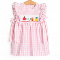  This dress features a pink check print, bows on the sides, and school supplies smocking. 