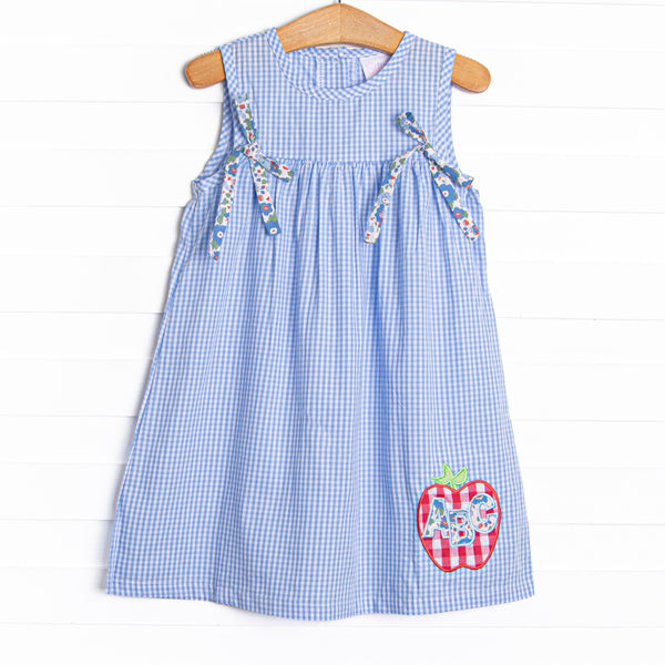 This dress features a blue gingham print, blue floral bows, and an apple applique.