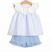  This dress featues a blue check print, a bib collar, and a floral embrodiery. Coordinating blue ruffle shorts to match! 