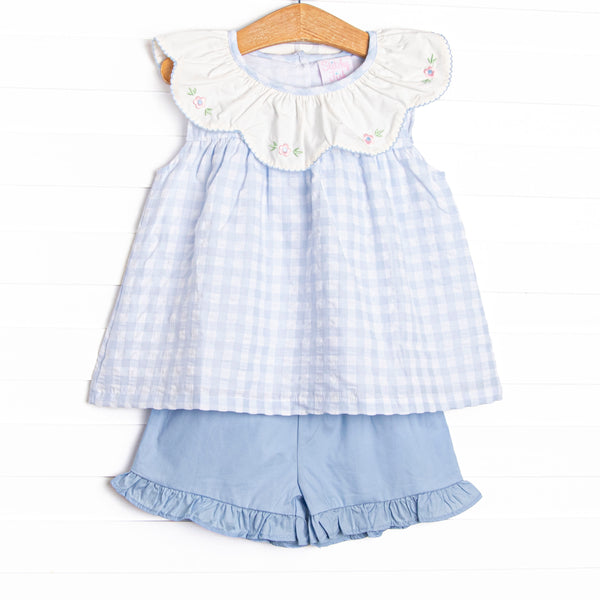  This dress featues a blue check print, a bib collar, and a floral embrodiery. Coordinating blue ruffle shorts to match! 