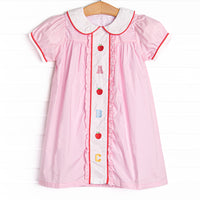 This dress features pink material, puff sleeves, and abc and apple embroidery.
