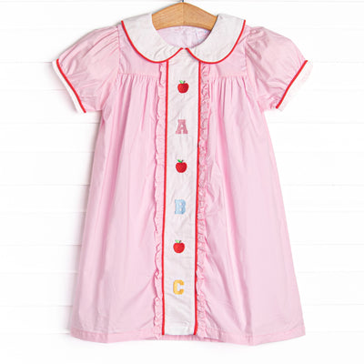 This dress features pink material, puff sleeves, and abc and apple embroidery.