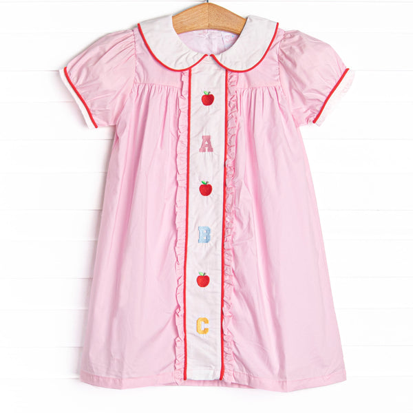 This dress features pink material, puff sleeves, and abc and apple embroidery.