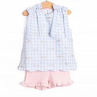 This dress featues a blue check print, shoulder ties, and a floral embrodiery. Coordinating pink ruffle shorts to match!