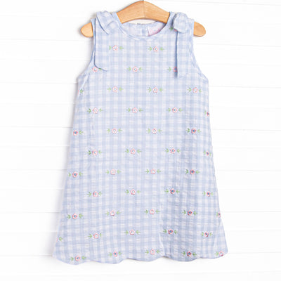 This dress featues a blue check print, scalloped trim, and a floral embrodieries.