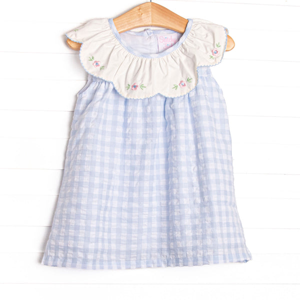 This dress featues a blue check print, a bib collar, and a floral embrodiery.