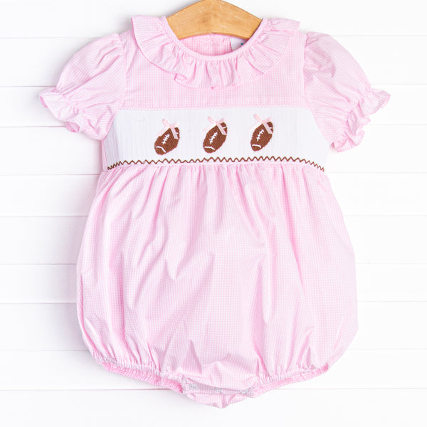 This bubble features a pink mini gingham print, a ruffle collar, and a trio of football smocking.