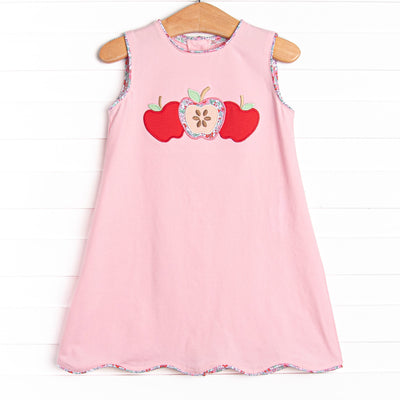 This dress features a pink knit material, scalloped trim, and a trio of apple appliques.