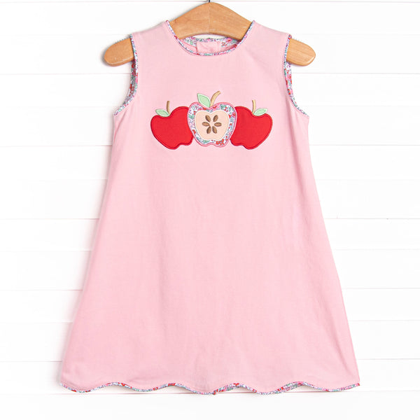 This dress features a pink knit material, scalloped trim, and a trio of apple appliques.