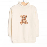 This sweater features white fabric, a rolled neck, and a teddy bear icon.