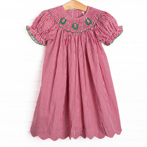 This dress features a red gingham print, puff sleeves, and a trio of wreath smockings.