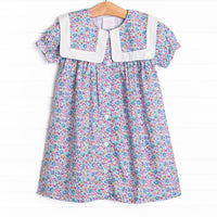 This dress features a purple floral print, a bib collar, and puff sleeves.