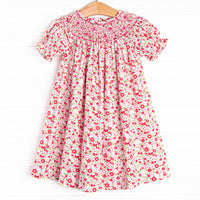 This dress features a pink floral print, buttons on the back, and a floral smocking.