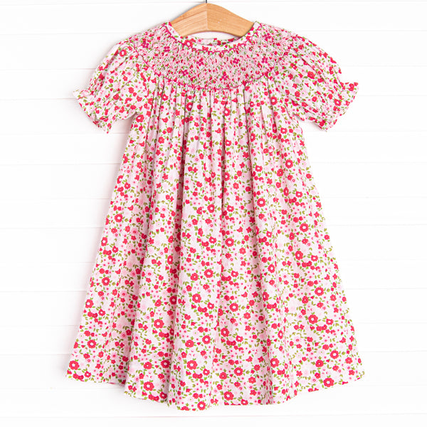 This dress features a pink floral print, buttons on the back, and a floral smocking.
